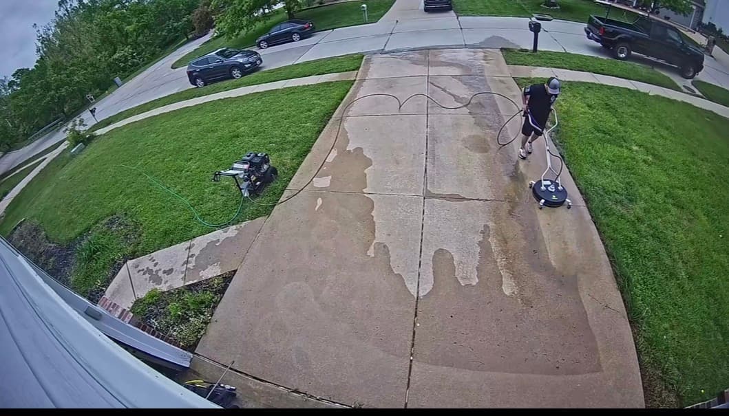 High-angle view of a person pressure washing a concrete driveway with a surface cleaner.