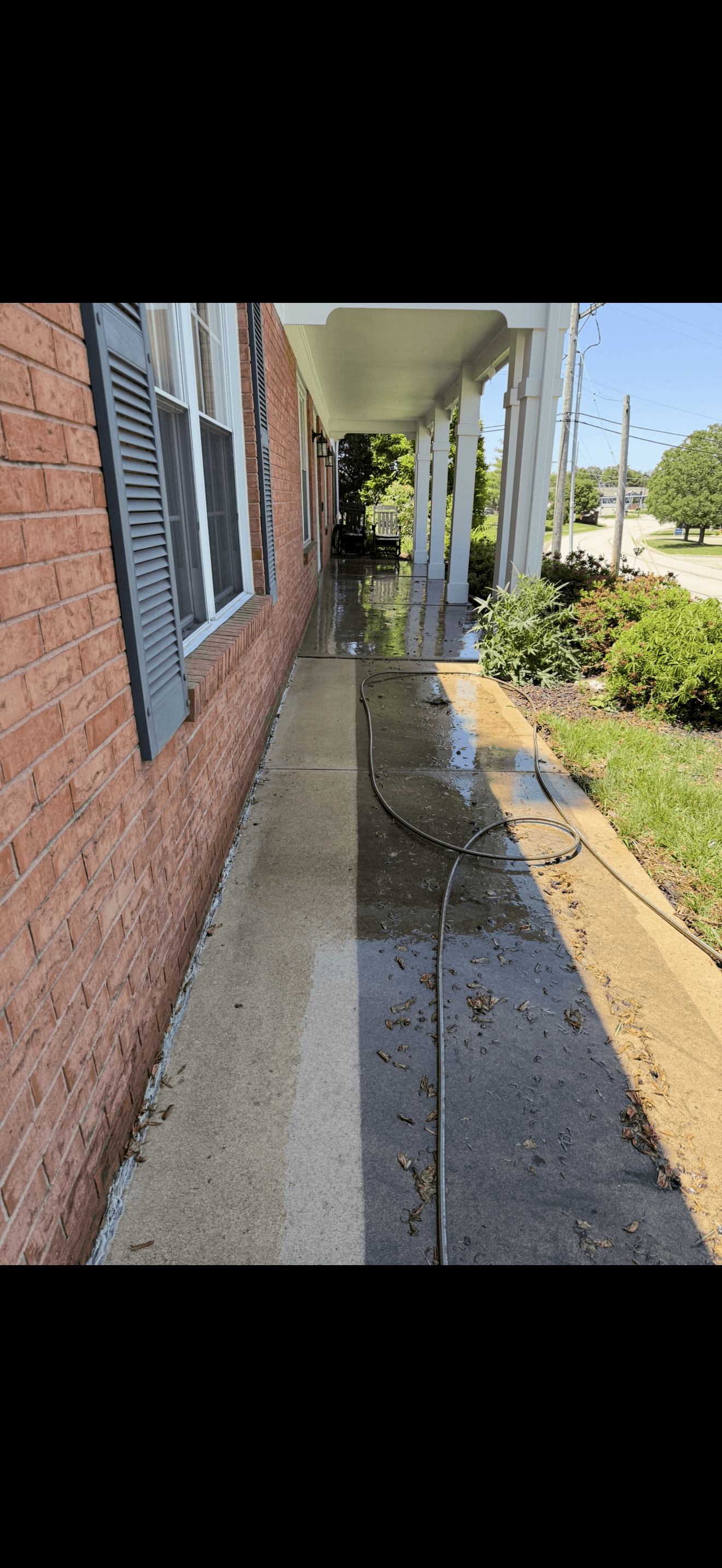 Partially power washed concrete walkway showing a clean and dirty contrast beside a brick house.